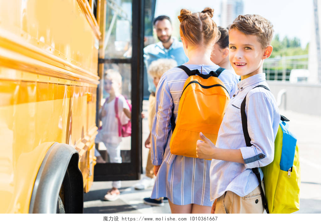 排队上校车的学生微笑的小男孩进入校车与同学, 而老师站在附近的门